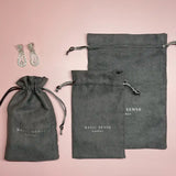 Grey drawstring dust bags with ’BASIC SENSE’ branding alongside crystal earrings.
