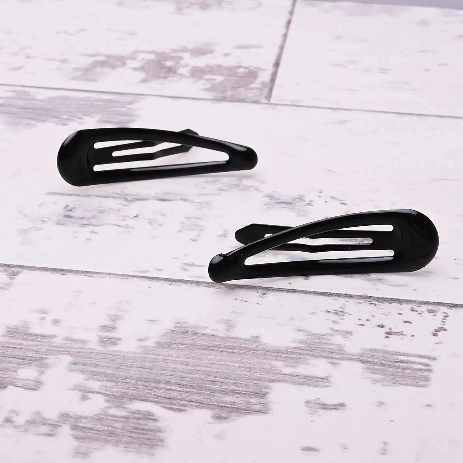 Two durable black metal hair clips on white wooden floor from Epoxy Metal Hair Clips set