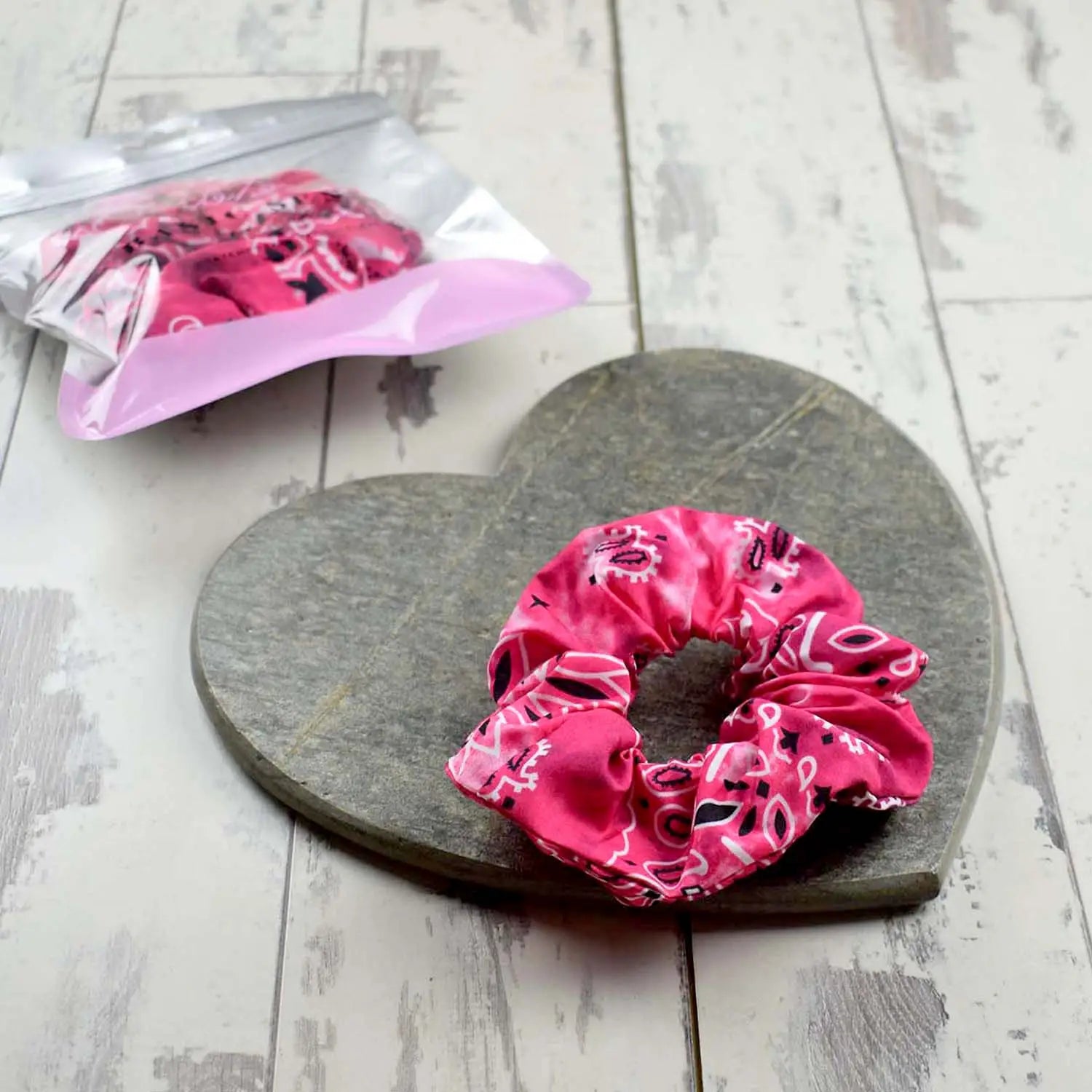 Fuchsia paisley scrunchie on a heart-shaped stone surface, with a coordinating transparent bag next to it.