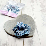 Scrunchie with a grey and white floral pattern, presented on a heart-shaped stone slab and plastic packaging.