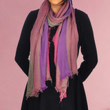 Woman wearing purple scarf and black top showcasing bold multicoloured striped scarf with frayed edges