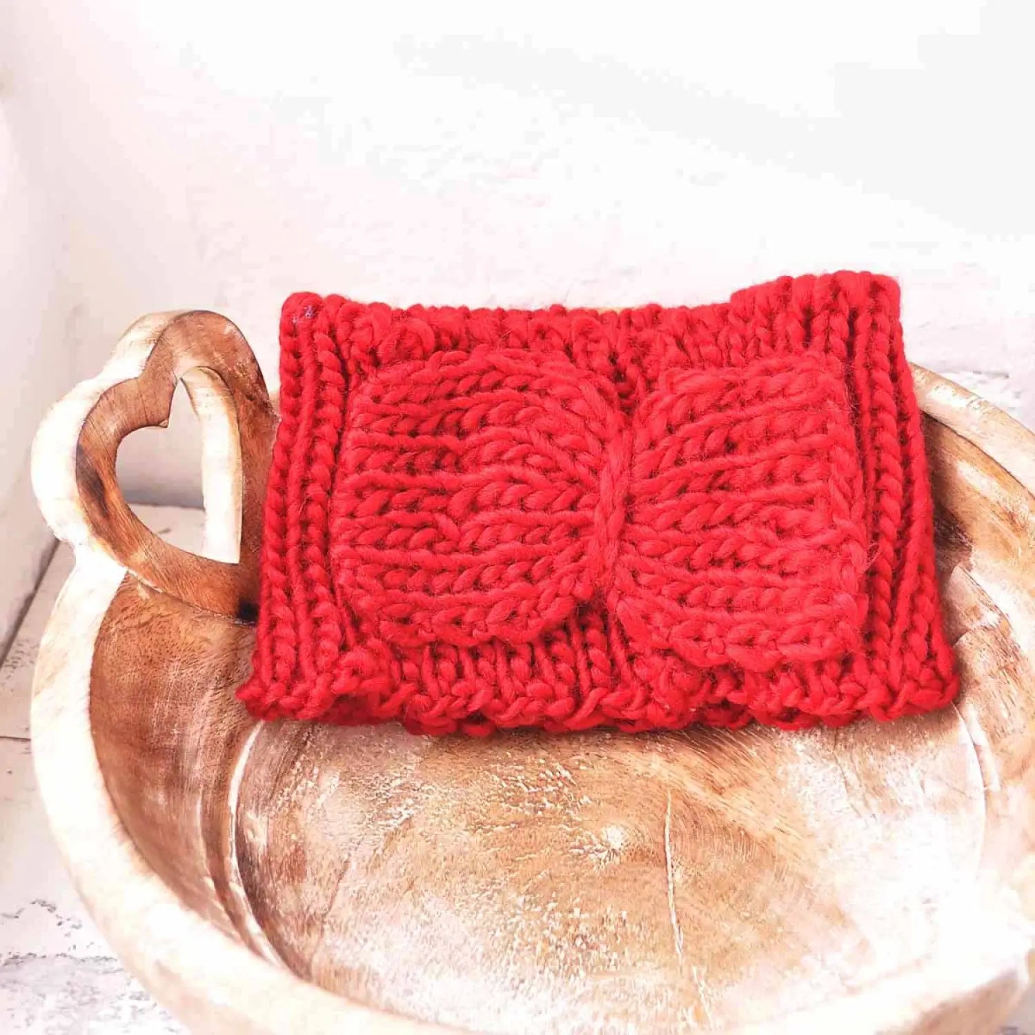 Red knitted scarf on wooden bowl, bow-detailed knitted headband for autumn & winter.