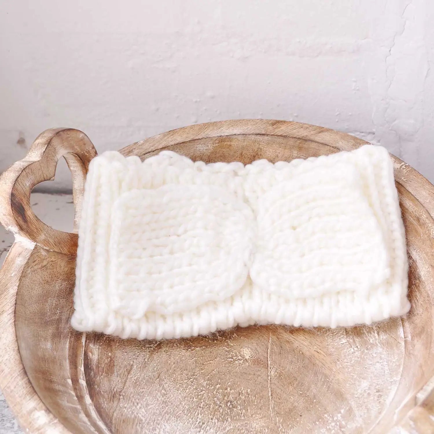 Stylish white knit headband with bow detail on wooden bowl