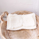 Stylish white knit headband with bow detail on wooden bowl