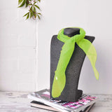 Green chiffon square scarf displayed on grey chair.