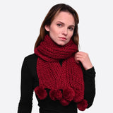 Chunky knit winter scarf with pom pom accents worn by woman in red scarf and black sweater