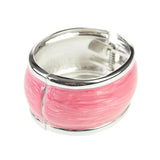 Pink enamel ring with silver band displayed on chunky pastel hinged bangle.