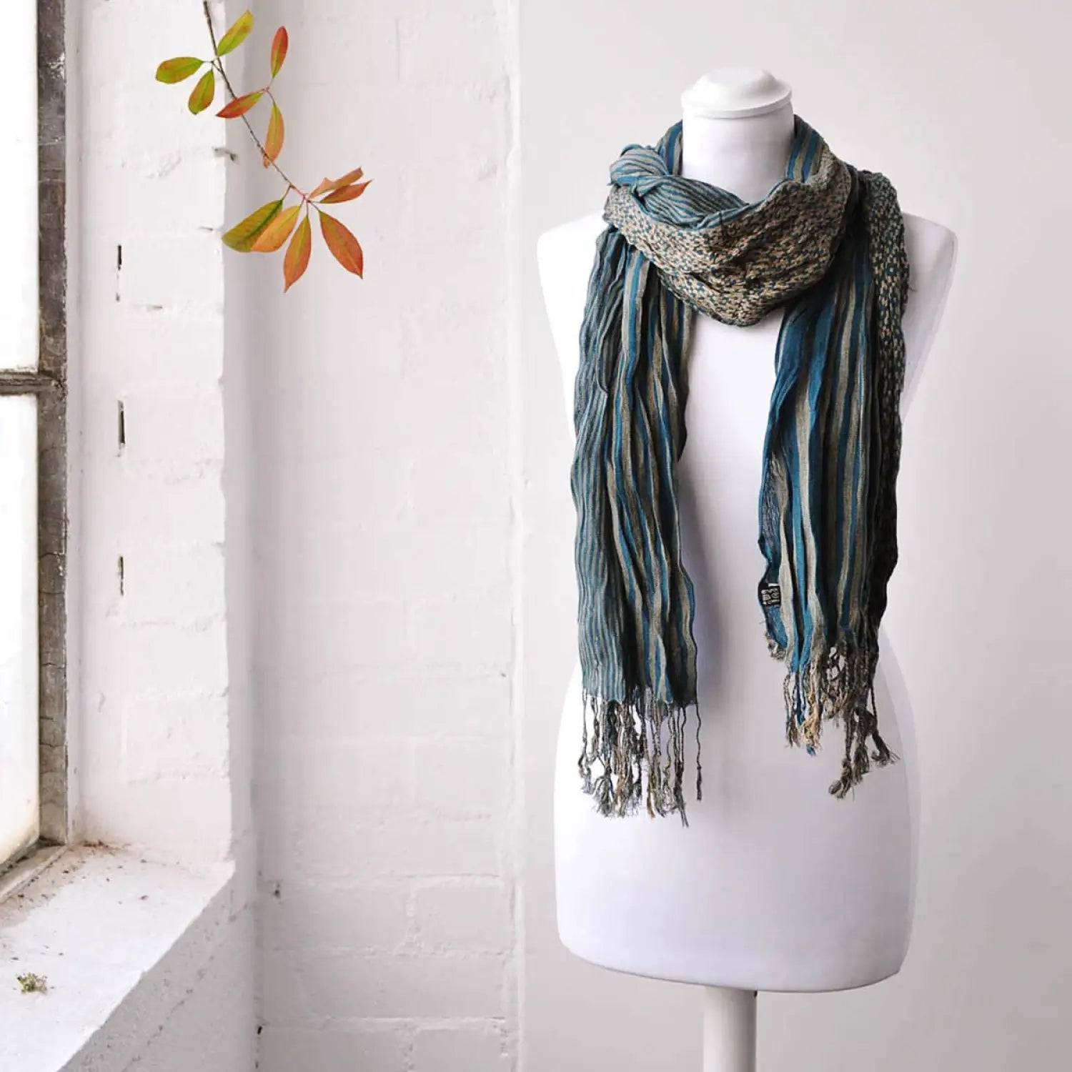 Mannequin showcasing Elegant Striped Woven Winter Scarf with playful bobble detail_near window