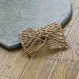 Gold bow hair clip accessory displayed on wooden floor from Glossy Beaded Design Hair Accessory Magic Comb.