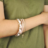 Woman wearing gold plated bracelet with pink flower, imitation pearl, and peach ribbon.