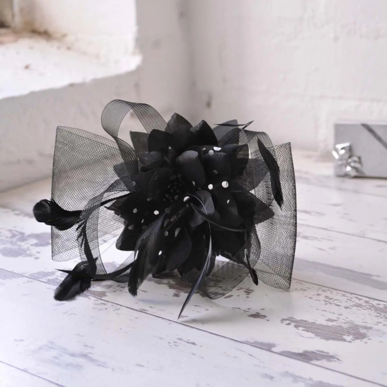 Black mesh flower and feather fascinator accessory comb on white table