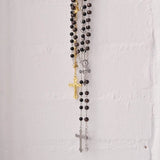 Metallic rosary beads necklace with saints pendant and cross on white wall