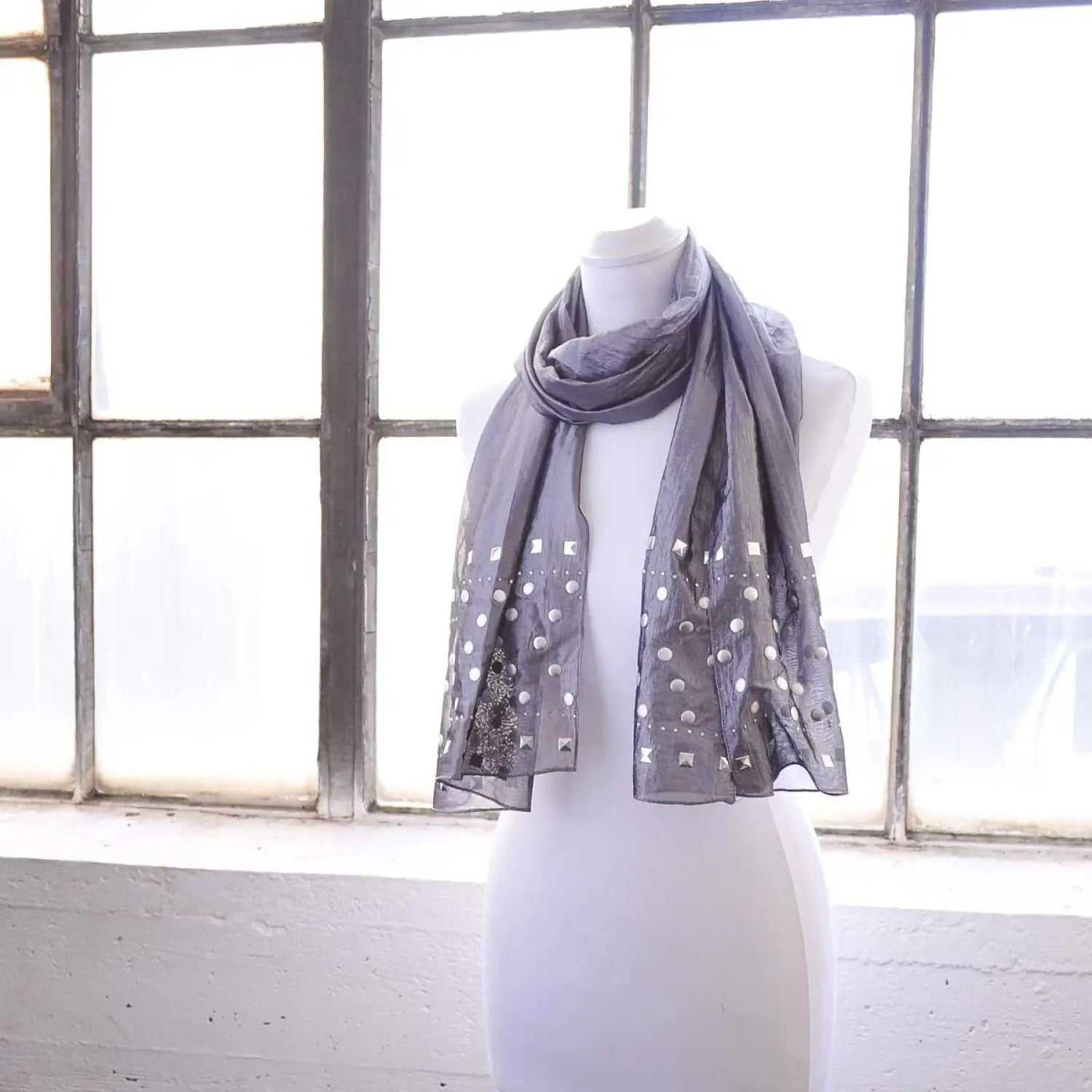 Metallic studded shimmering lightweight scarf draped on mannequin in front of window.