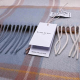 A plaid wool scarf in muted beige, light blue, and soft grey tones, featuring a 'Basic Sense' tag indicating its inclusion in their 'Wool Collection'. Laid out on a smooth, light surface, this scarf is crafted from 100% high-quality Mongolian wool.
