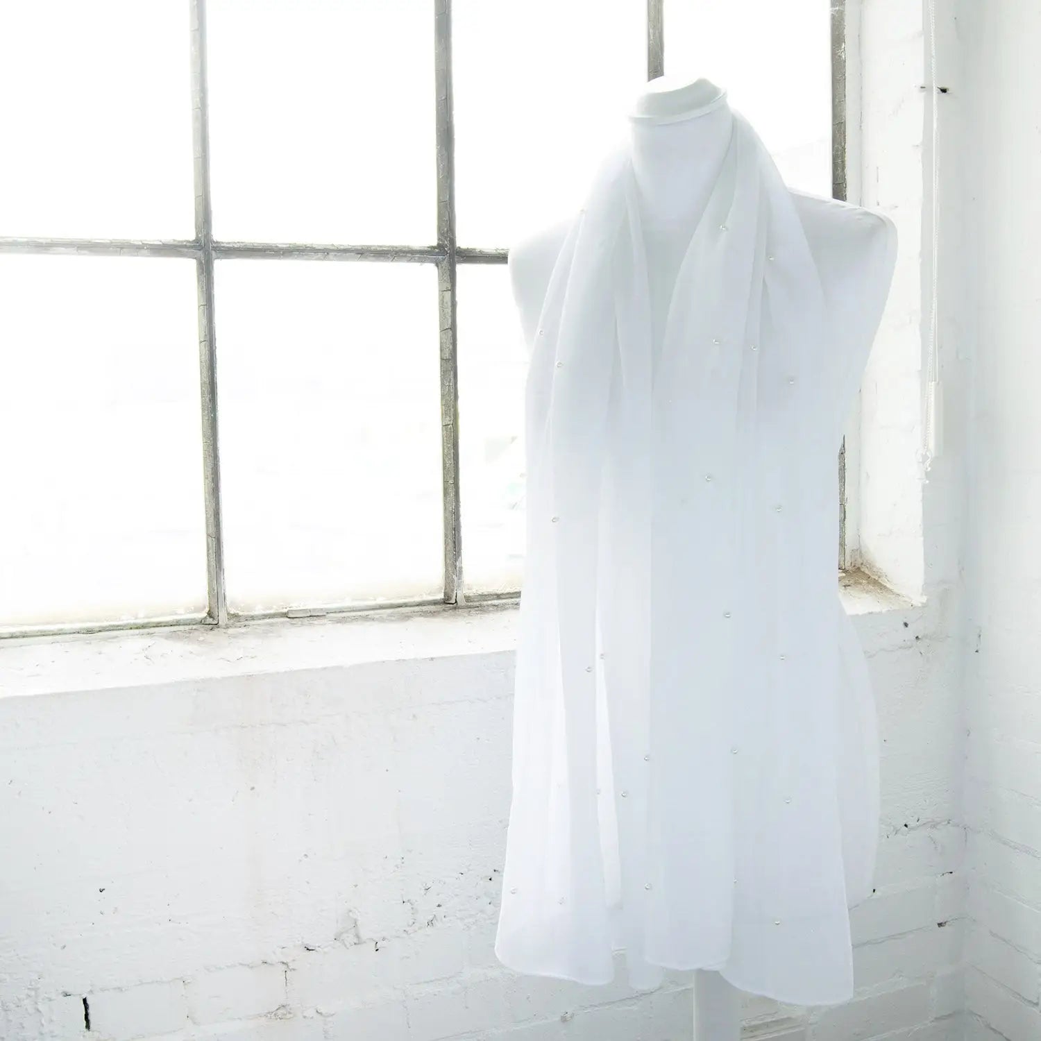 White dress hanging on window side, showcasing Pearl Chiffon Scarf with Durable Pearl Attachments