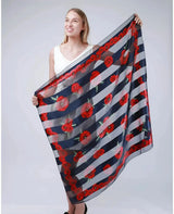 Woman holding a large square poppy scarf with red flowers.