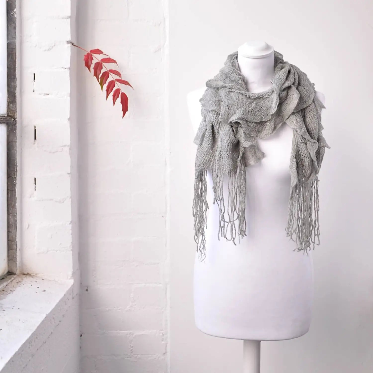 Lightweight knitted ruffled scarf on mannequin with red leaf background