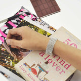 Person holding book with sparkling stone cuff bracelet and chocolate bar in background